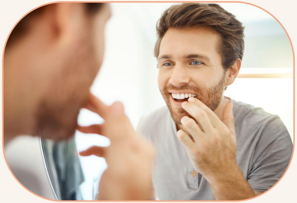 man touching his teeth in mirror at inspired smiles